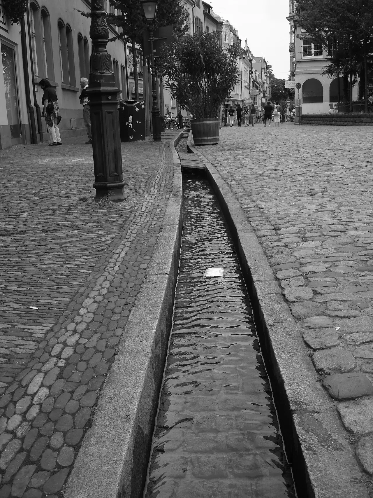 ร่องน้ำ Freiburger Bächle ตามพื้นถนนหินในเมืองเก่า ภาพขาวดำ ภาพจาก Wikimedia Commons ผู้ถ่าย Jaanaa74 สัญญา CC BY-SA 3.0 ปีที่ถ่ายไม่ระบุ