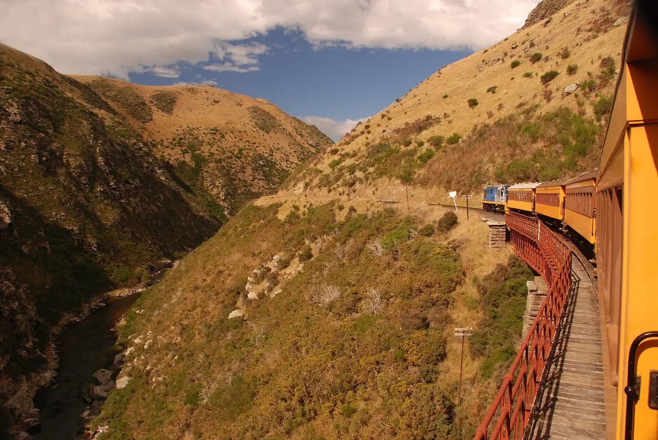 ขบวนรถไฟ Taieri Gorge วิ่งเลียบหุบเขาและสะพานโลหะข้างลำธาร ภาพจาก Wikimedia Commons ผู้ถ่าย Mike Goren สัญญา CC BY 2.0 ไม่ระบุปีที่ถ่าย