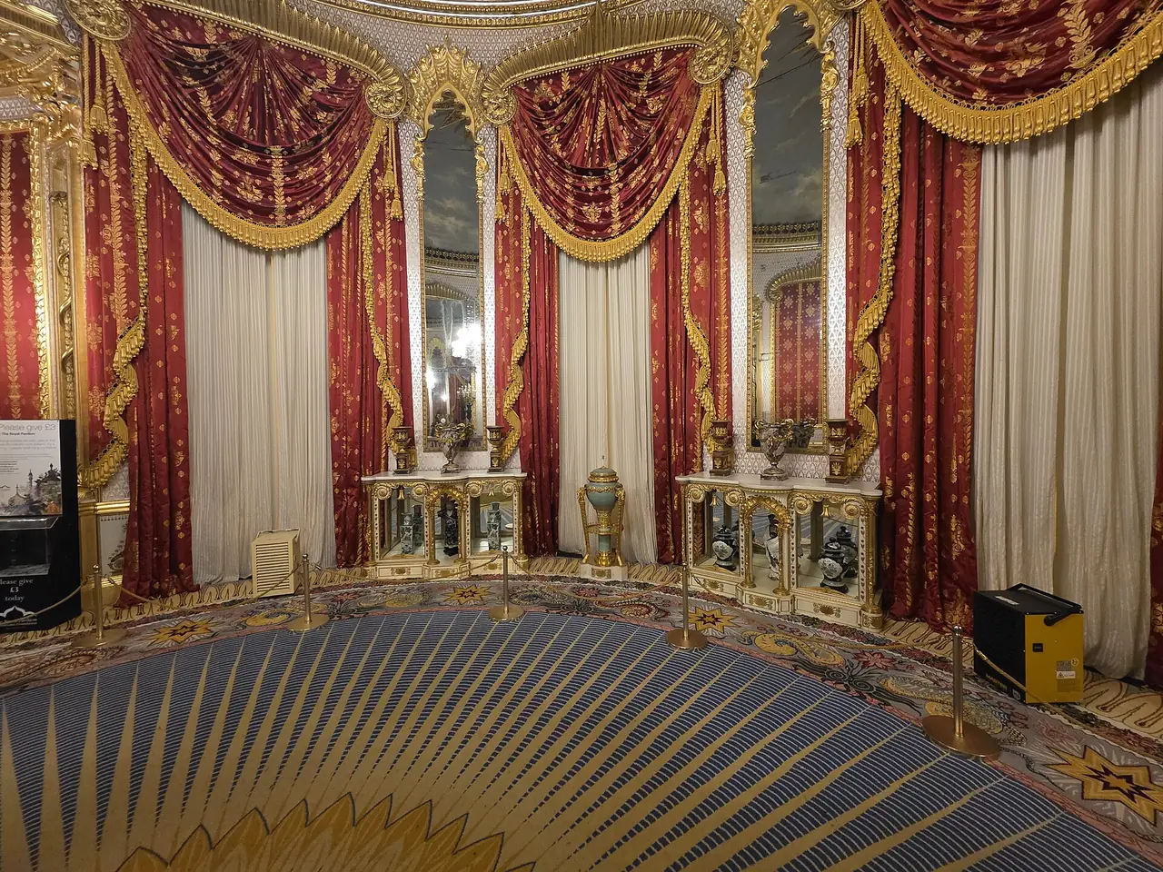 ห้องวงกลมตกแต่งม่านสีแดงและพรมลายรัศมีในพระราชวัง ภาพจาก Wikimedia Commons ผู้ถ่าย HJ Mitchell สัญญา CC BY 4.0 ไม่ระบุปีที่ถ่าย ผู้ถ่ายระบุว่าเป็นภายใน Royal Pavilion