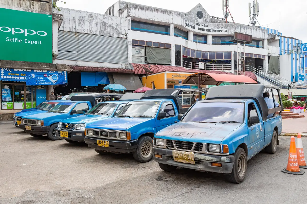 รถสองแถวสีฟ้าจอดรอที่ตัวเมืองตราด ด้านหลังเป็นอาคารตลาด ภาพจาก Wikimedia Commons ผู้ถ่าย Ilya Plekhanov สัญญา CC BY-SA 4.0 เป็นภาพประกอบ ไม่ระบุปีที่ถ่าย
