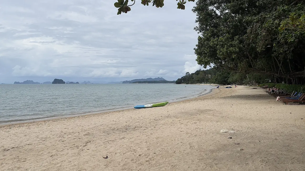 หาดทับแขกที่เห็นทะเลเรียบ ต้นไม้ร่มริมฝั่งและเกาะหินปูนไกล ๆ ภาพจาก Wikimedia Commons ผู้ถ่าย Stefan Fussan สัญญา CC BY-SA 4.0 ไม่ระบุปีที่ถ่าย ตามชื่อไฟล์คือหาดทับแขก กระบี่ ซึ่งบล็อกบอกว่าลานจอดรถทางขึ้นอยู่ใกล้หาดนี้ เป็นภาพประกอบของบริเวณใกล้ทางเข้า ไม่ใช่ตัวเขา