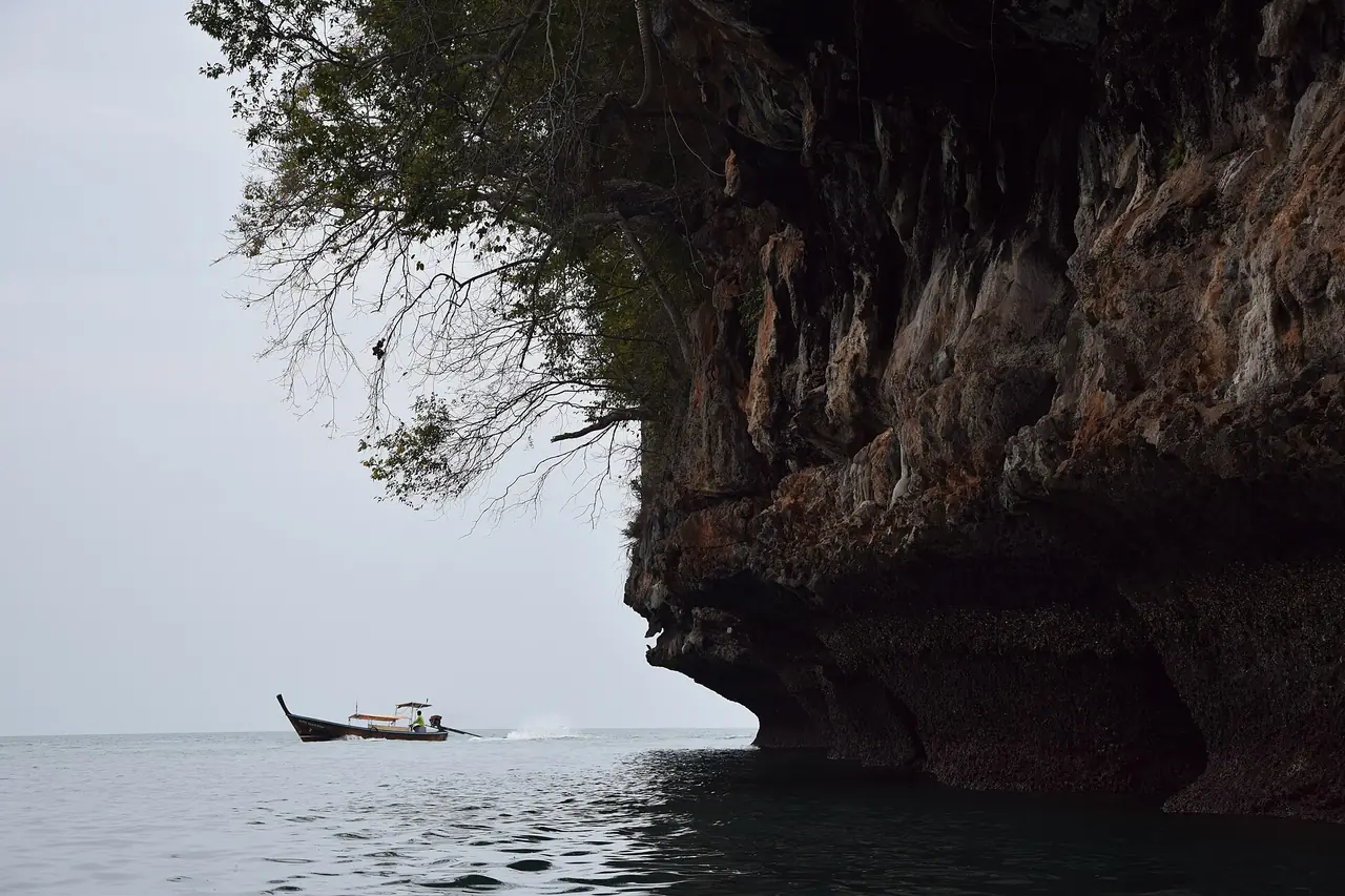 หน้าผาหินปูนที่ยื่นเหนือทะเลสะท้อนเงามืด มีเรือหางยาวแล่นอยู่ไกล ๆ ภาพจาก Wikimedia Commons ผู้ถ่าย Victor Belousov สัญญา CC BY 3.0 ชื่อไฟล์ระบุตำบลหนองทะเล อำเภอเมืองกระบี่ ไม่ระบุปีที่ถ่ายและจุดที่แน่นอน เป็นภาพประกอบของพื้นที่ใกล้เคียง ไม่ใช่ตัวเขา