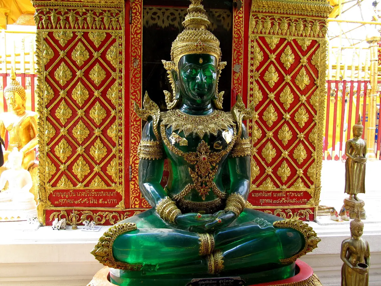 พระพุทธรูปสีเขียวหยกประดับทองในซุ้มสีแดงทองที่วัดพระธาตุดอยสุเทพ ภาพจาก Wikimedia Commons ผู้ถ่าย Dinkum สัญญา CC0 ภาพนี้ไม่ลงวันที่ถ่ายและเป็นภาพประกอบ เรายังไม่ยืนยันชื่อและประวัติของพระองค์นี้