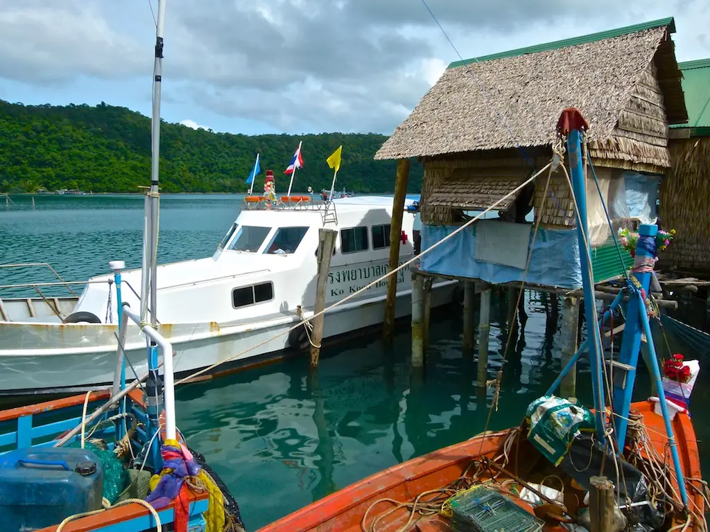 เรือเร็วสีขาวจอดเทียบสะพานกระท่อมมุงจากข้างเรือประมงสีส้มในหมู่บ้านอ่าวสลัด ตามชื่อไฟล์บน Commons เป็นภาพ Ban-Aosalad เรือเร็วในภาพเป็นเรือท้องถิ่นที่ไม่ได้ระบุว่าเป็นของบริษัทใด ภาพจาก Wikimedia Commons ผู้ถ่าย josef knecht สัญญา CC BY 3.0