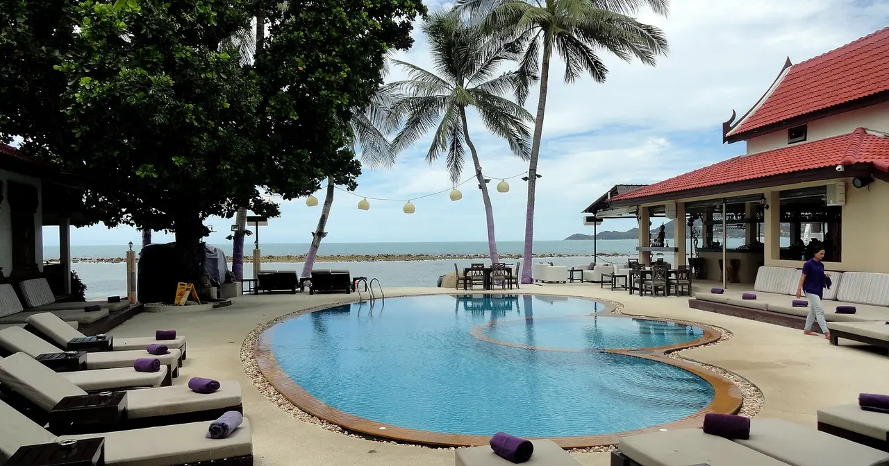 สระว่ายน้ำของรีสอร์ตริมทะเล มีเก้าอี้นอนและร้านอาหารกึ่งเปิดโล่ง ภาพที่ Commons ติดป้ายหาดเฉวง ไม่ทราบว่าเป็นรีสอร์ตใดและปีใด ใช้เป็นภาพประกอบลักษณะที่พักริมหาด ไม่ใช่การแนะนำรีสอร์ต ภาพจาก Wikimedia Commons ผู้ถ่าย Fabio Achilli สัญญา CC BY 2.0