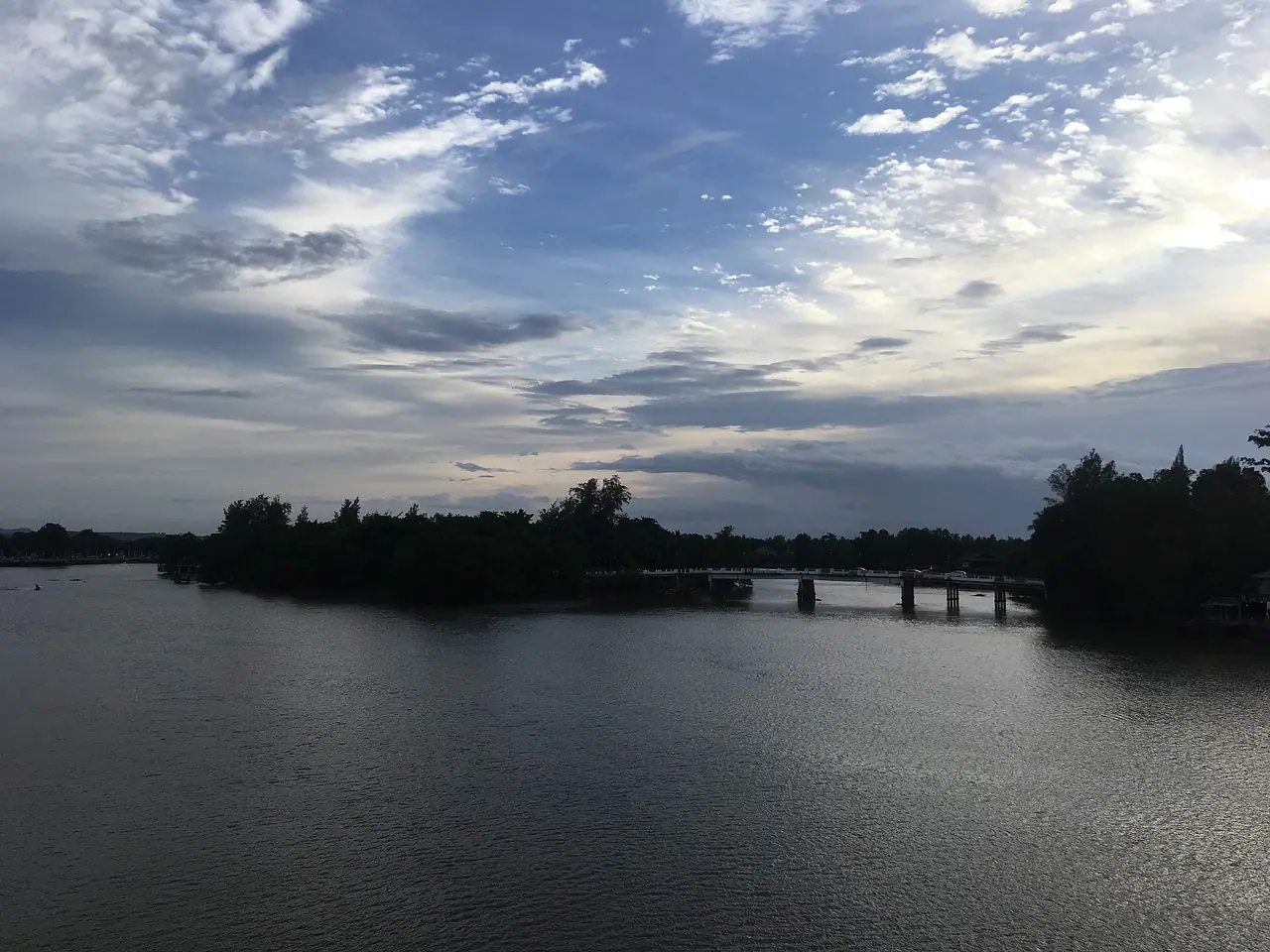 แม่น้ำตาปีตอนเย็น เห็นเงาต้นไม้บนเกาะและสะพานไม้ยาวเลียบน้ำ ภาพจาก Wikimedia Commons ผู้ถ่าย Christophe95 สัญญา CC BY-SA 4.0 ไม่ระบุปีที่ถ่าย ชื่อไฟล์ว่าเป็นภาพเกาะลำพูจากสะพานข้ามแม่น้ำตาปี