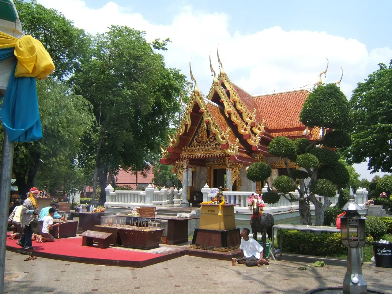 ศาลสมเด็จพระเจ้าตากสินมหาราช เมืองตาก หลังคากระเบื้องส้มและช่อฟ้าทอง มีผู้คนนั่งกราบด้านหน้า ภาพจาก Wikimedia Commons ผู้ถ่าย Media lib สัญญา CC BY-SA 4.0 ไม่ระบุปีที่ถ่ายในคำอธิบายไฟล์ ศาลอาจปรับปรุงไปแล้ว